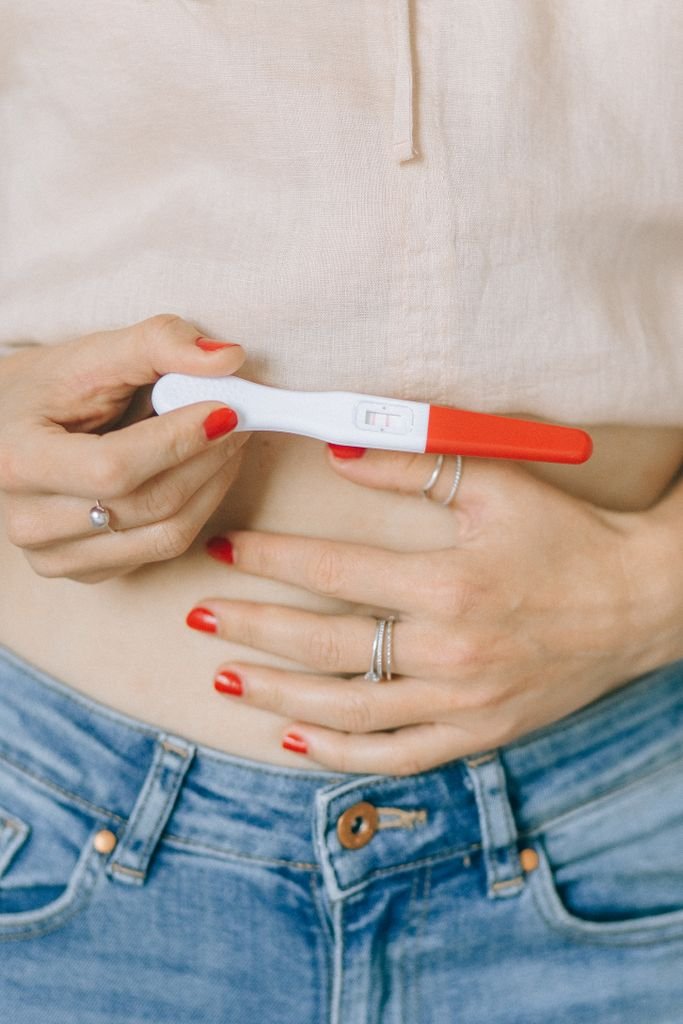 Close-up of a woman's hands holding a pregnancy test, showcasing red nail polish and rings.